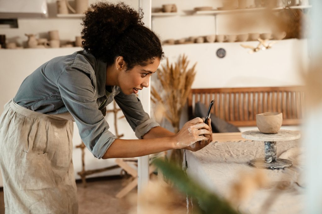 Black ceramist woman taking photo while working at her studio